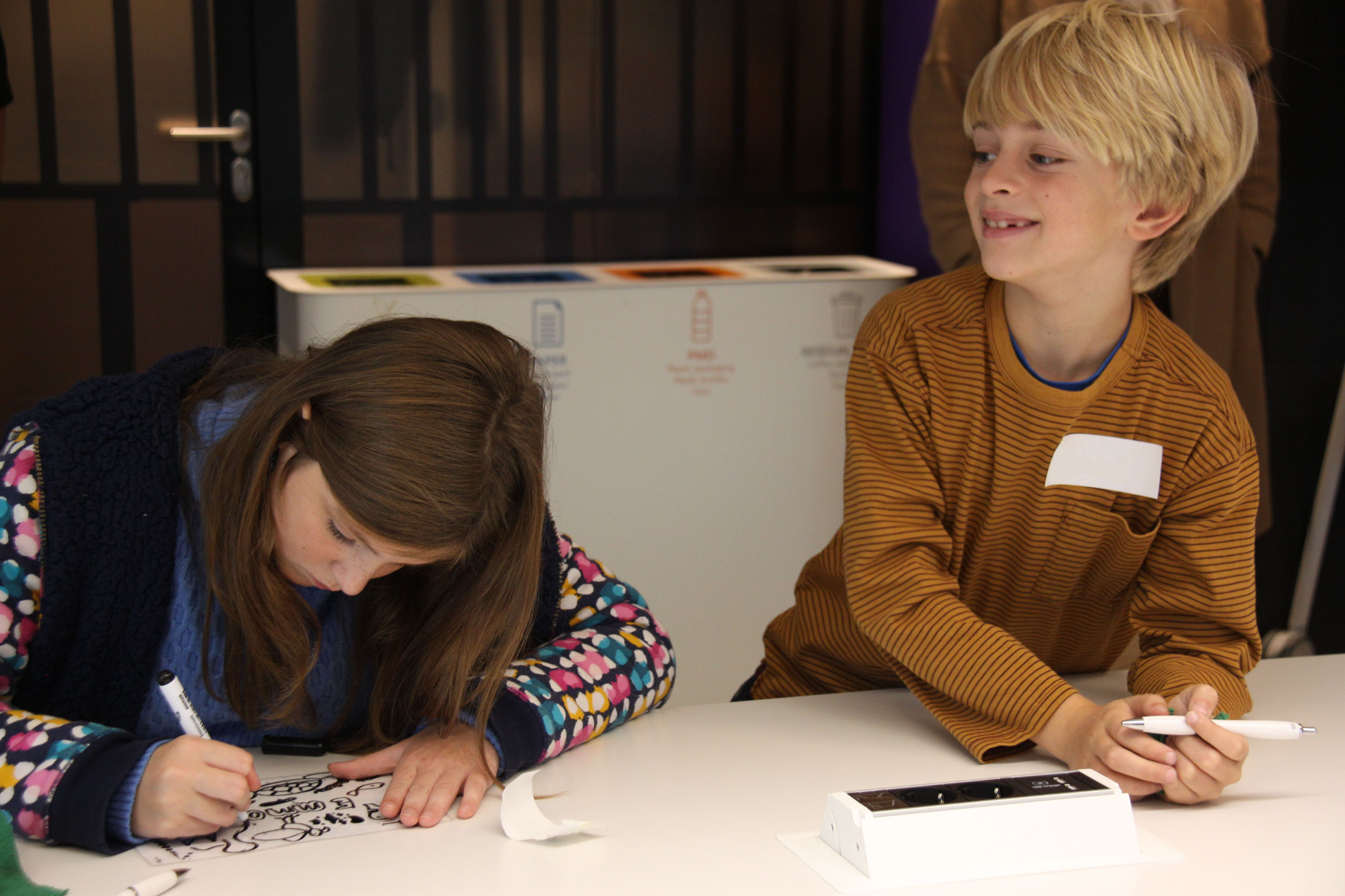 Een meisje tekent op papier en een jongen glimlacht