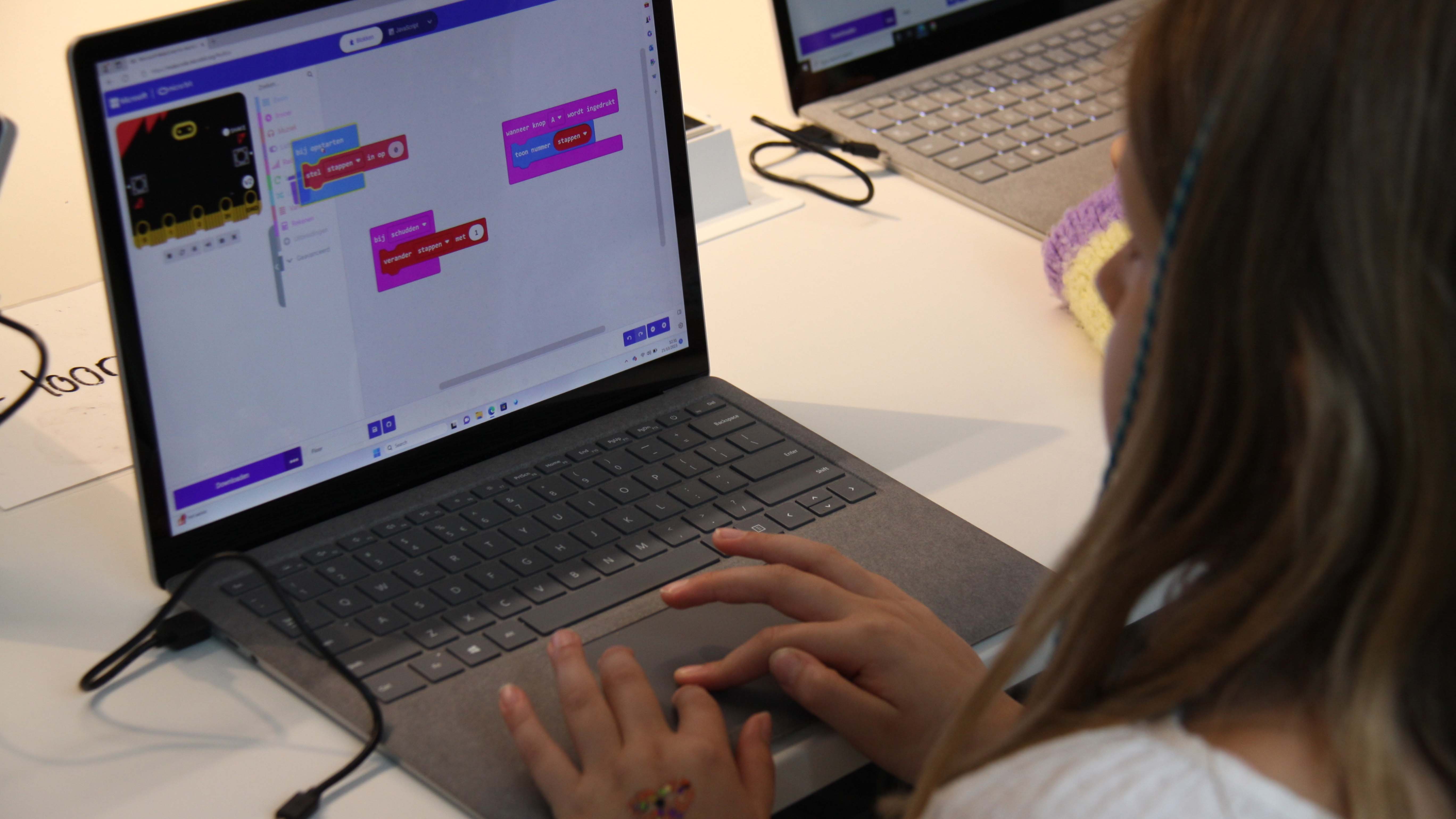 Een meisje werkt op een laptop, het scherm toont de MakeCode website